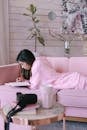 A Woman in a Pink Hoodie Taking Notes while Lying Down on a Couch
