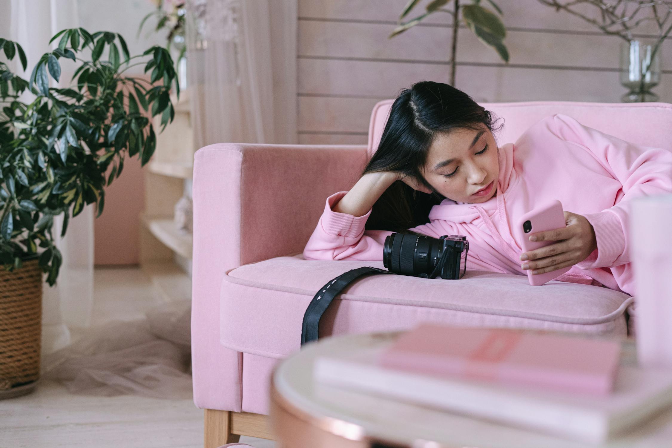 Person in a pink hoodie lying on a pink sofa with a pink phone case.