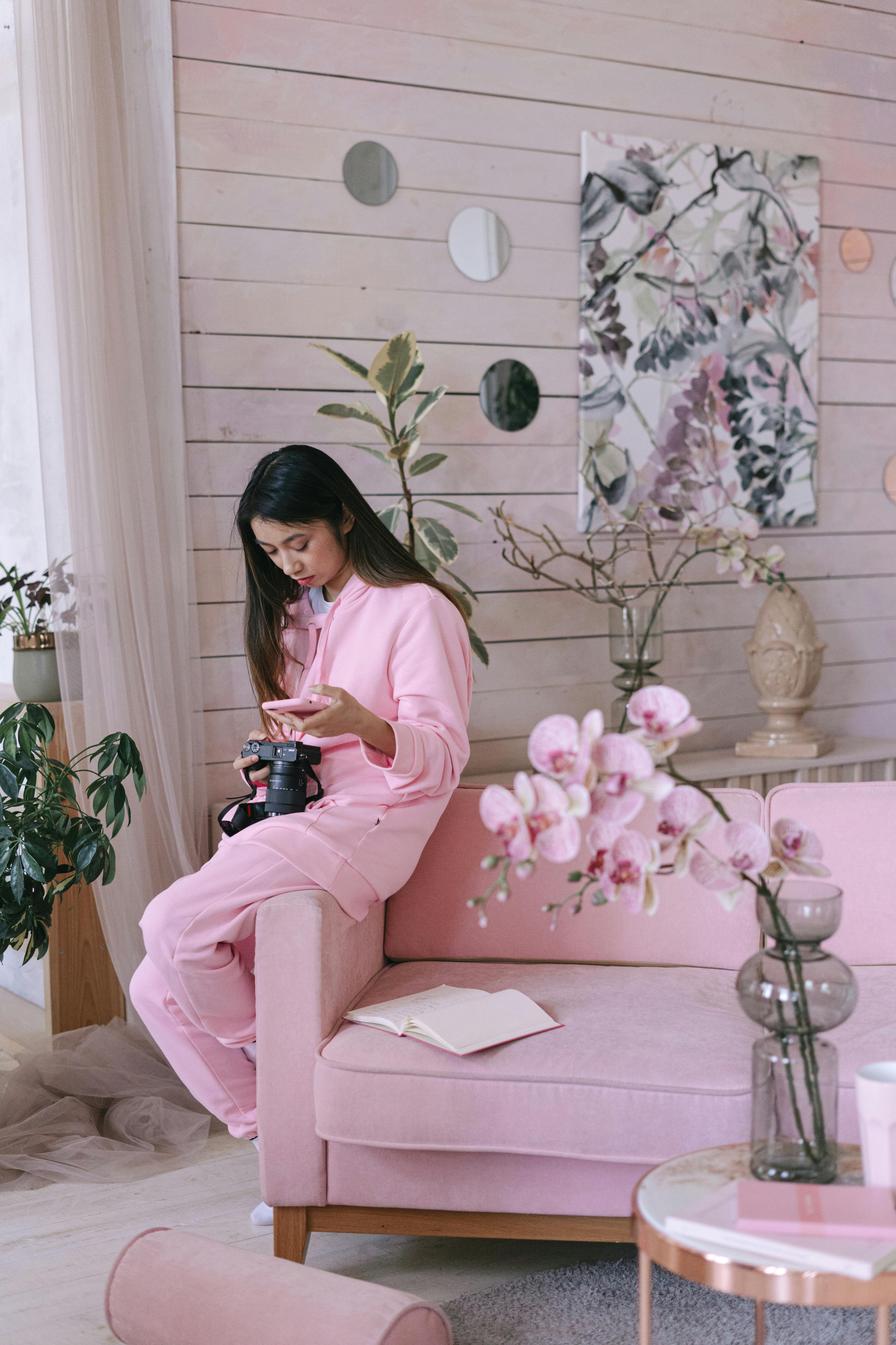 a woman in pink clothes sitting on the couch while holding a black camera