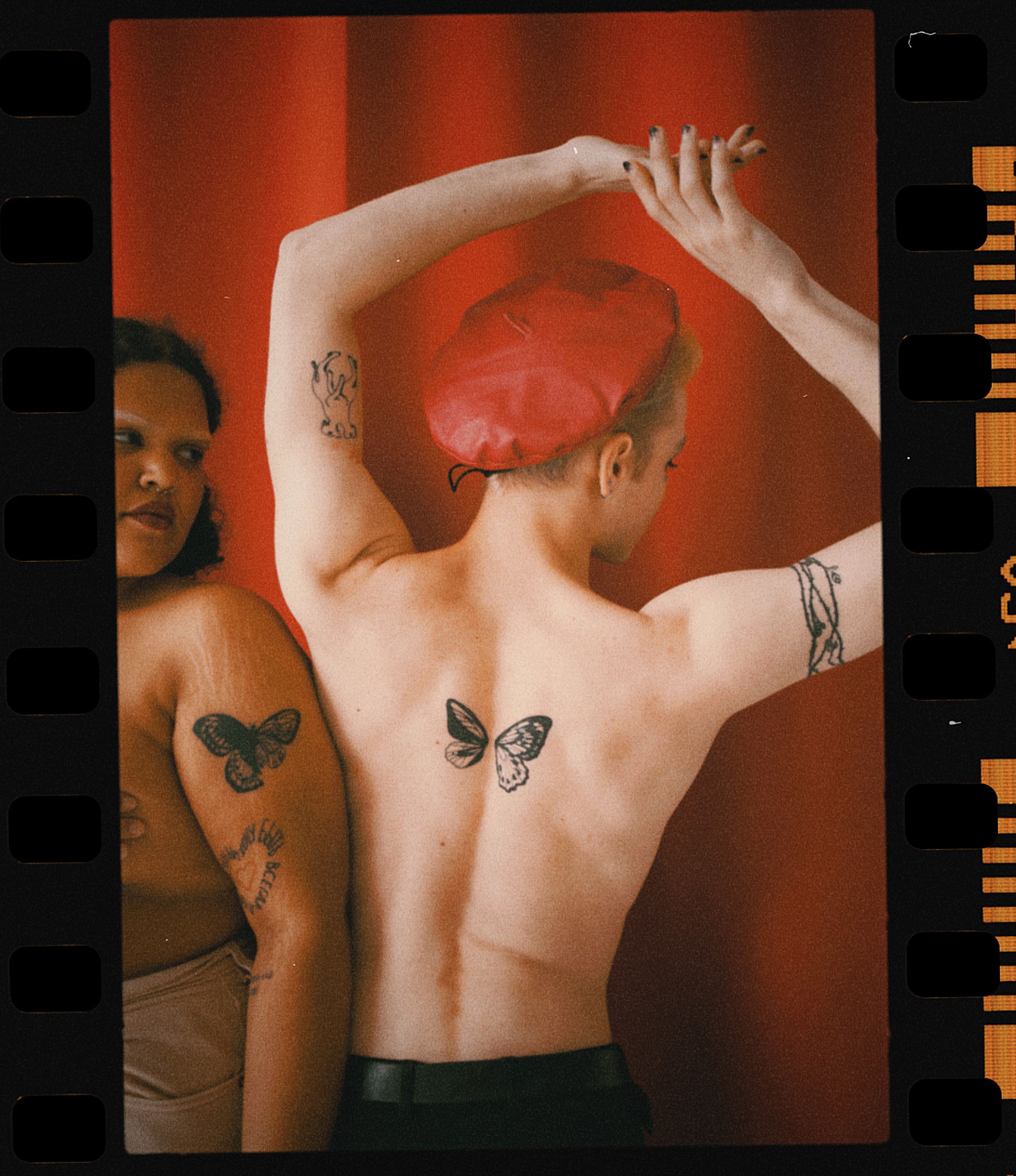 Photograph of two tattooed individuals embracing identity against a vivid red backdrop.