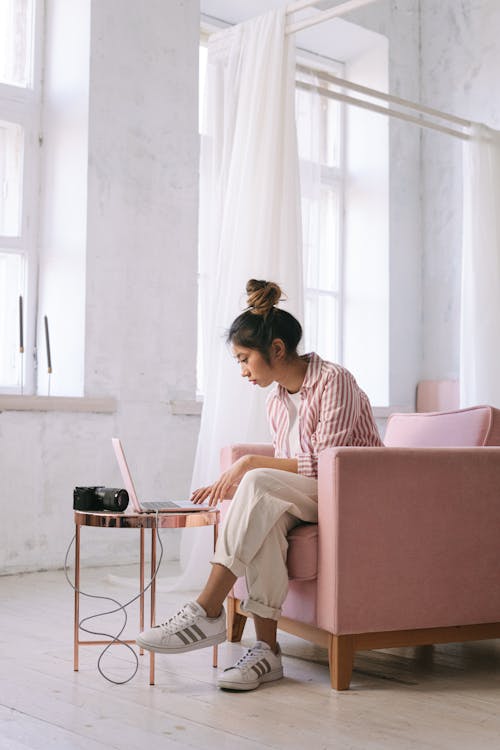 Free A Woman in Striped Shirt Sitting on the Chair while Working on Her Laptop Stock Photo