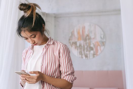 A young woman in a striped shirt using her smartphone indoors with soft decor and a relaxed atmosphere.
