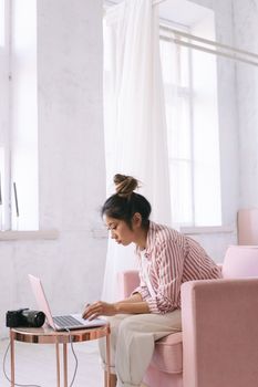 A woman focuses on her laptop in a modern, sunlit room, embodying a work-from-home setup.