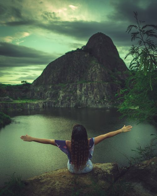 Free A woman enjoys nature with arms stretched wide, overlooking a tranquil mountain lake. Stock Photo