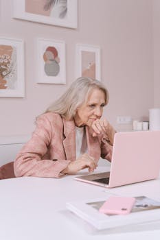 Senior woman in a cozy interior working on a pink laptop, showcasing modern technology.