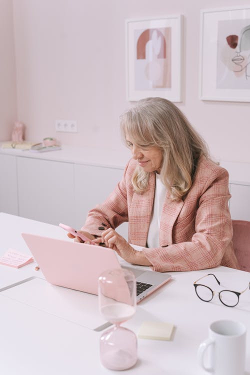 A Woman in a Pink Blazer Using Her Smartphone in Her Office