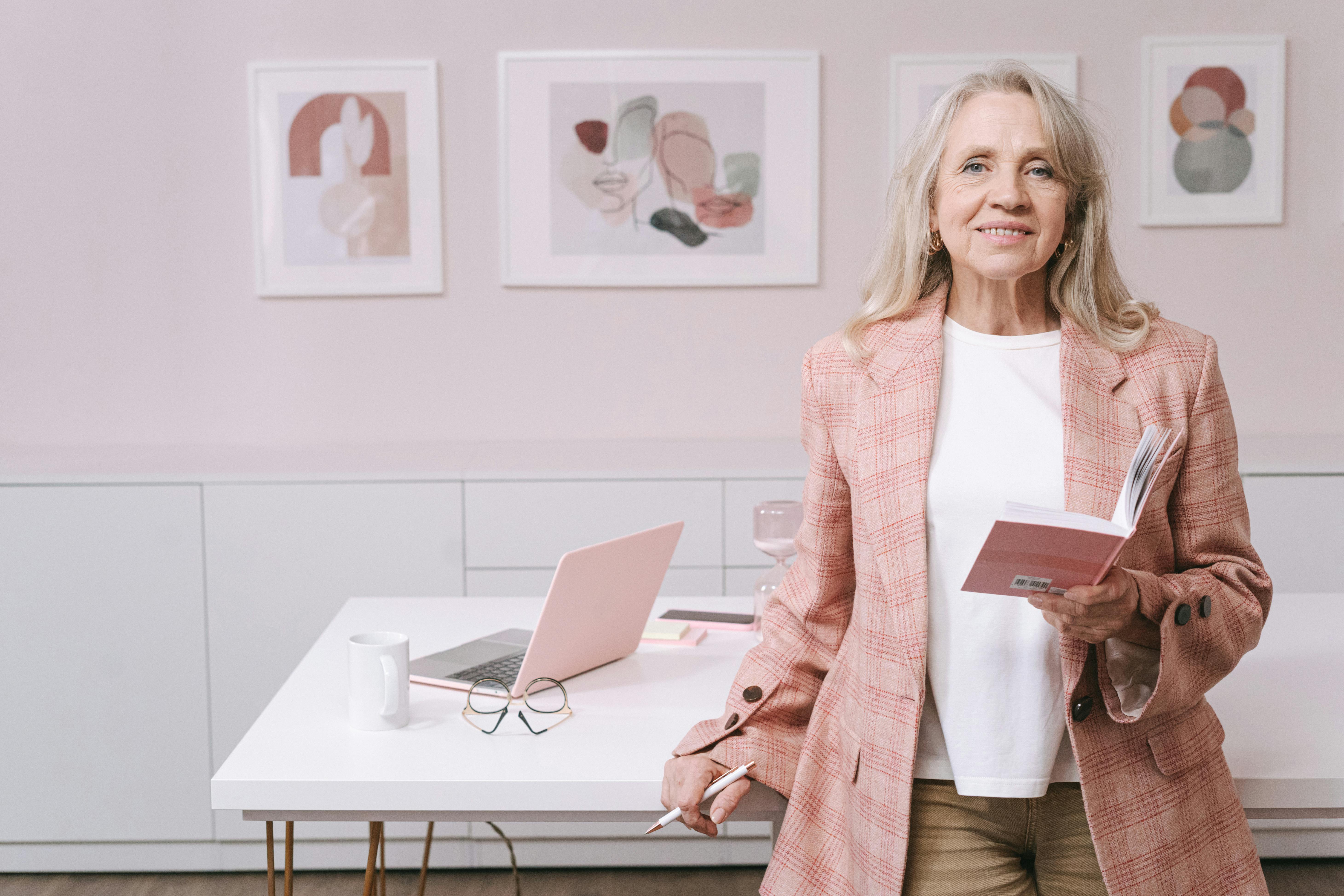 an elderly woman in pink blazer smiling while holding a book