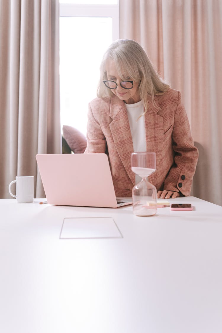 An Elderly Woman In Pink Coat Using Her Laptop On The Table