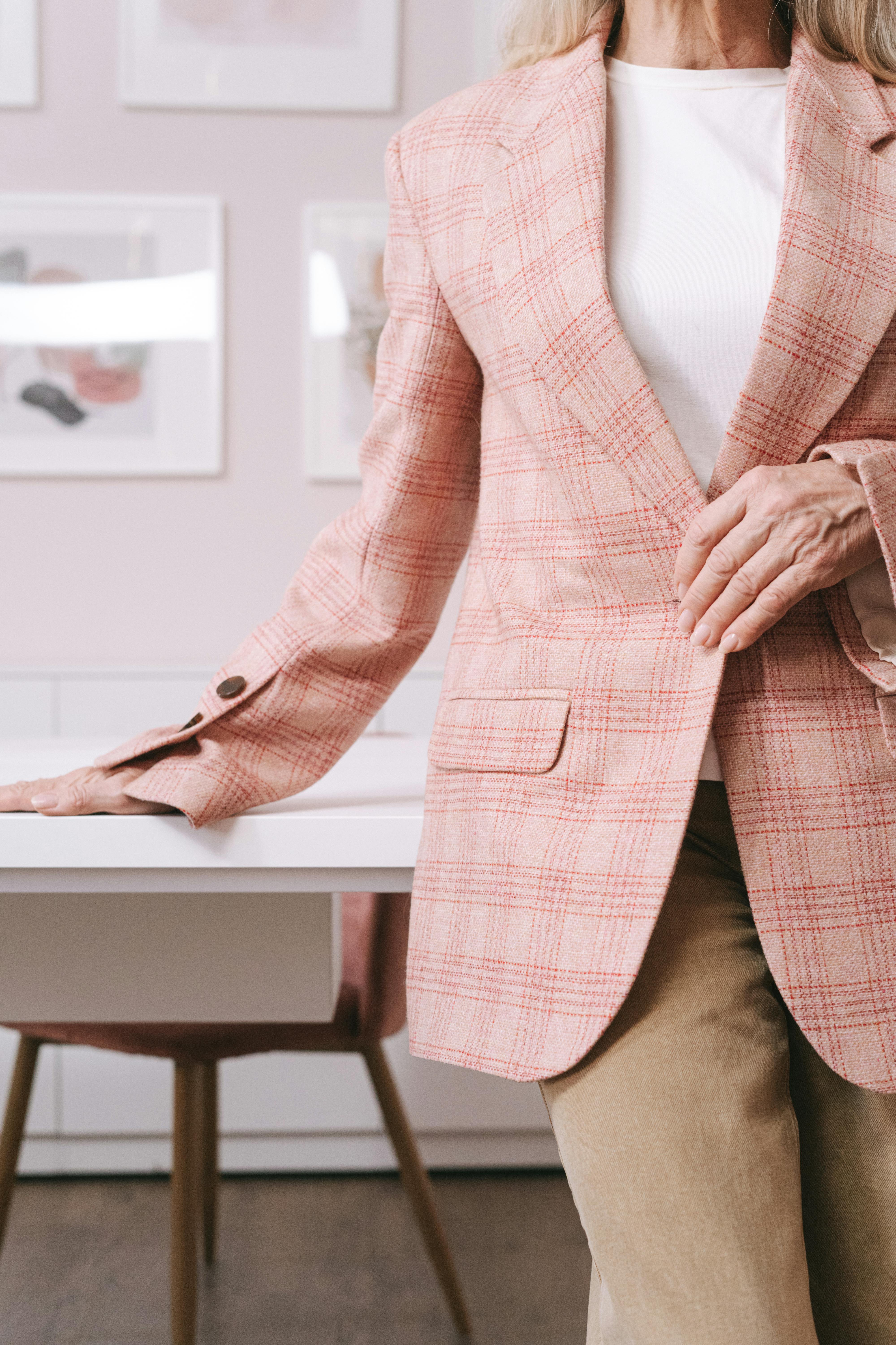 woman in pink and white plaid blazer sitting on brown wooden chair