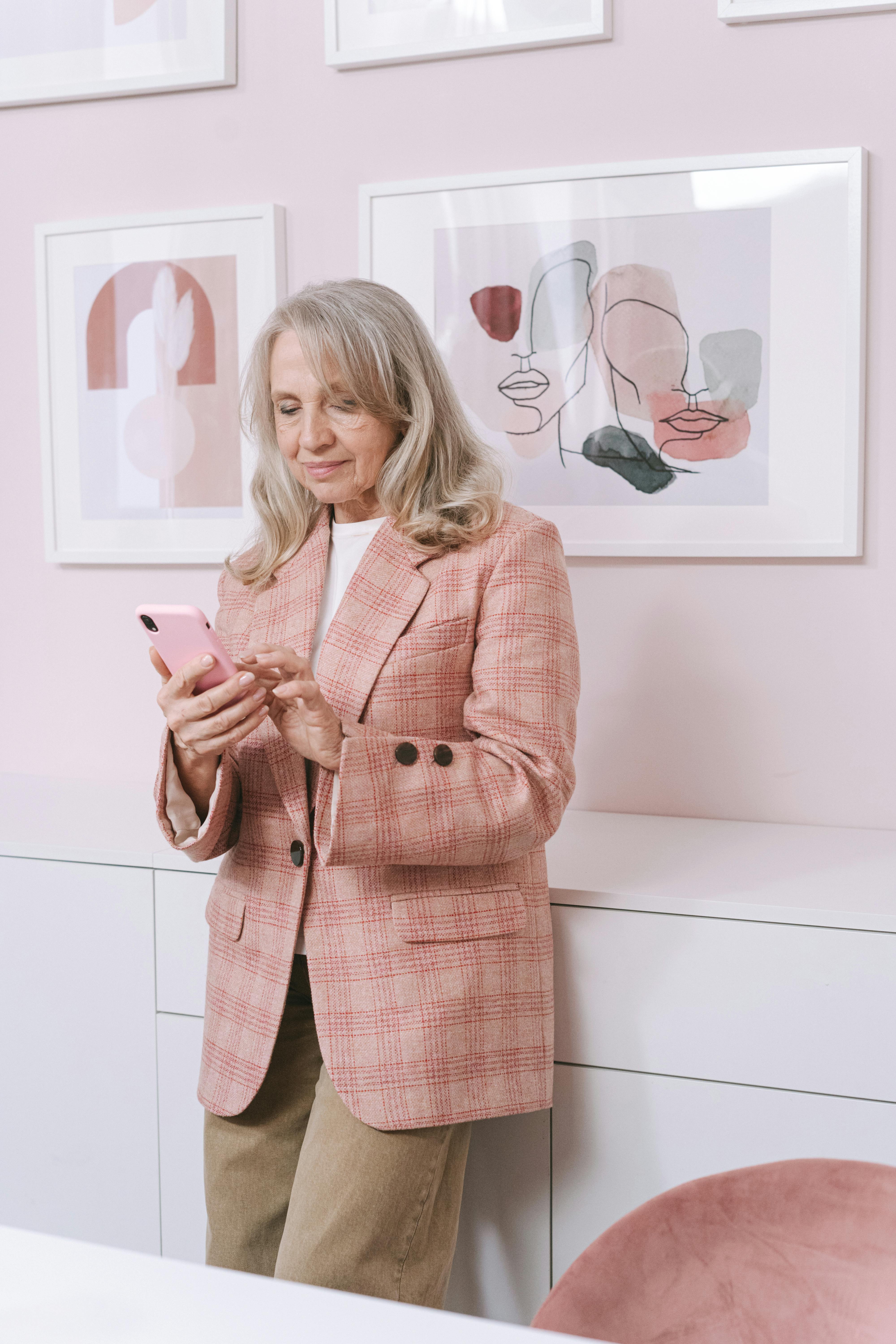 an elderly woman in pink coat standing while using her mobile phone