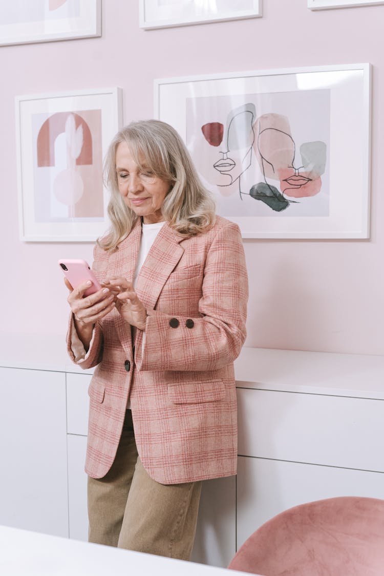 An Elderly Woman In Pink Coat Standing While Using Her Mobile Phone