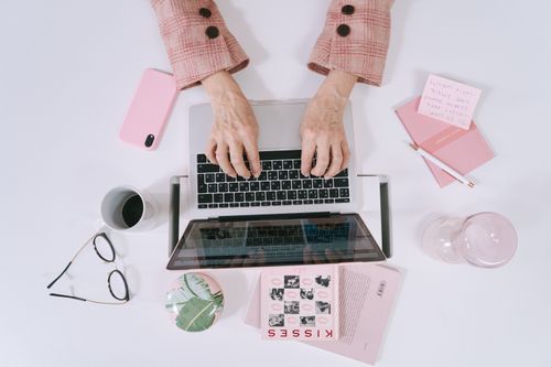 Free Stylish overhead shot featuring hands typing on a laptop with pink office accessories for a chic workspace vibe. Stock Photo