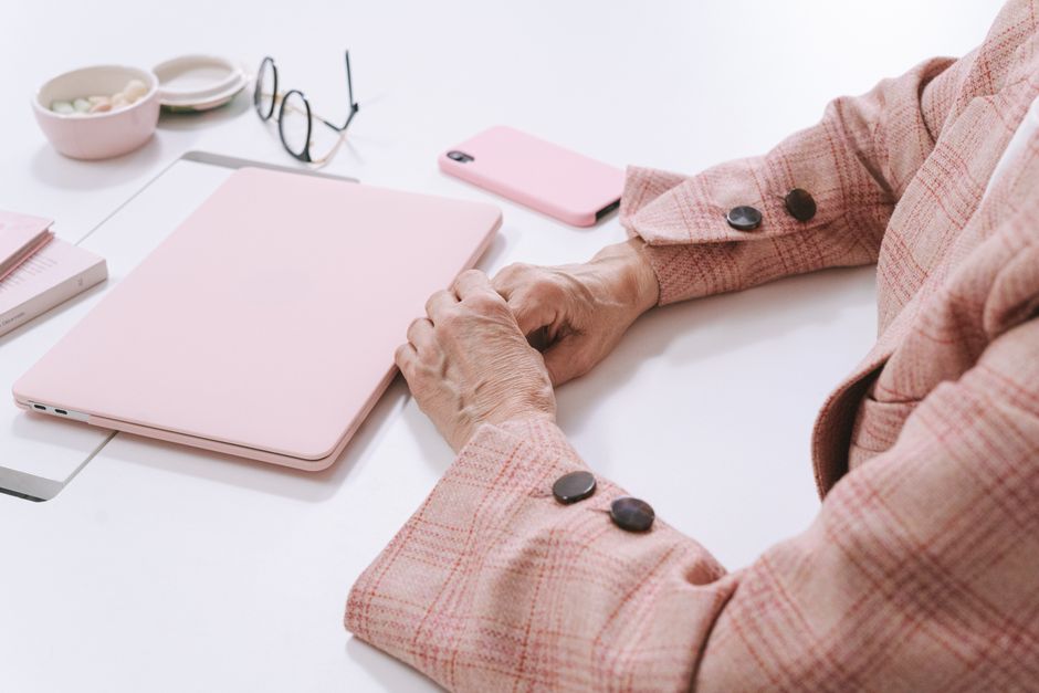 Un espacio de trabajo elegante con un portátil rosa, un teléfono inteligente y gafas sobre una mesa blanca, enfatizando la elegancia y la…
