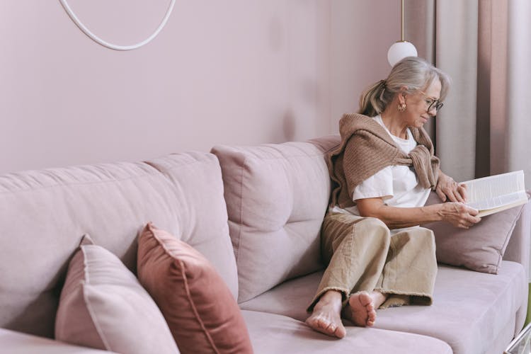 Photo Of An Elderly Woman Reading A Book On A Couch