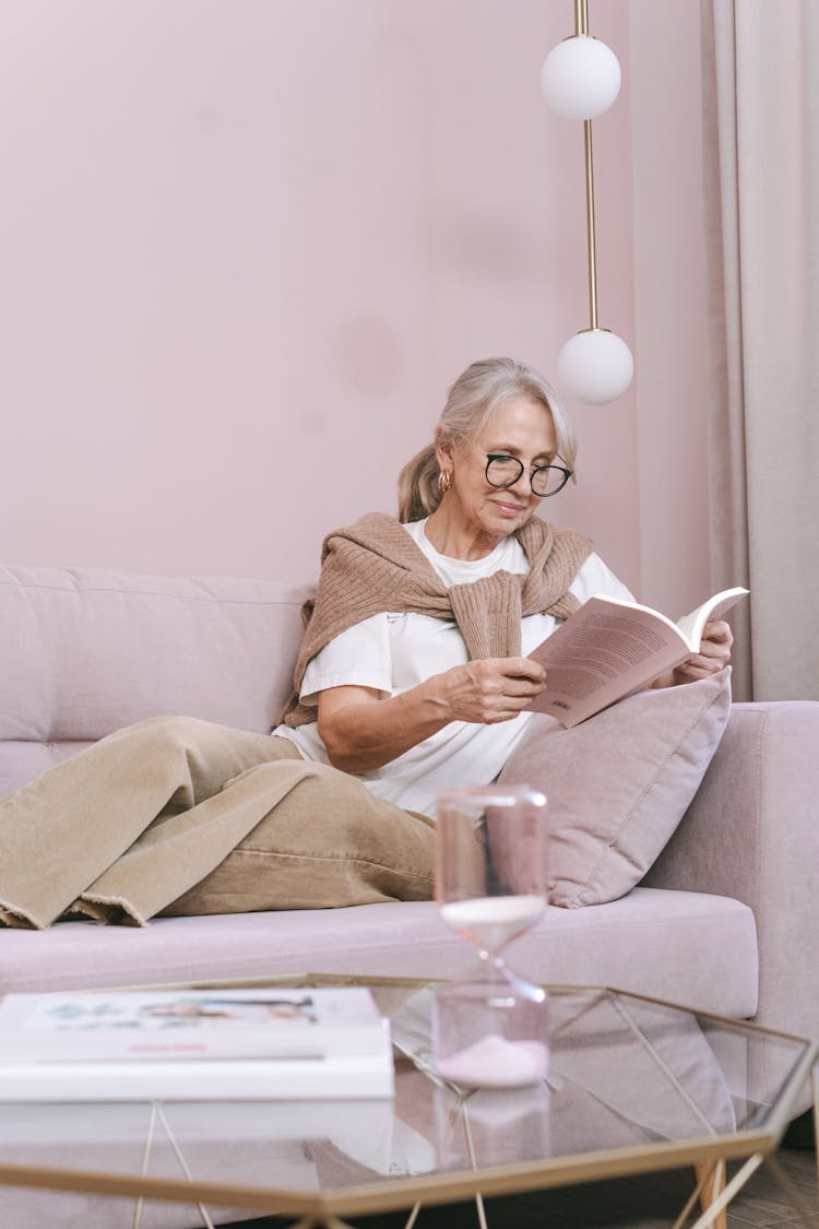 An Elderly Woman Reading A Book On A Sofa