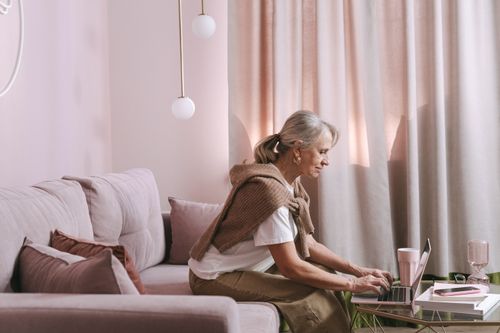 Free Elderly woman typing on a laptop in a cozy living room setting. Stock Photo