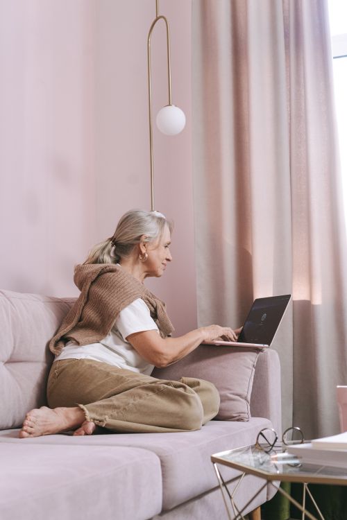 Free Elderly woman working remotely from a cozy home environment on a laptop. Stock Photo