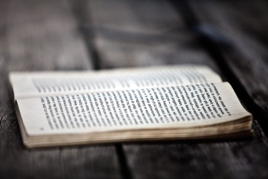 A close-up of an open book placed on a weathered wooden surface, with text in focus.