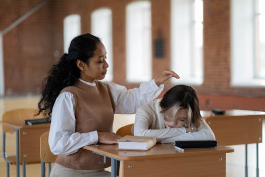 Two women in a classroom, offering support and comfort at a desk.
