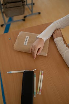 A student sitting at a wooden desk with a literature textbook and pens, ready to study.
