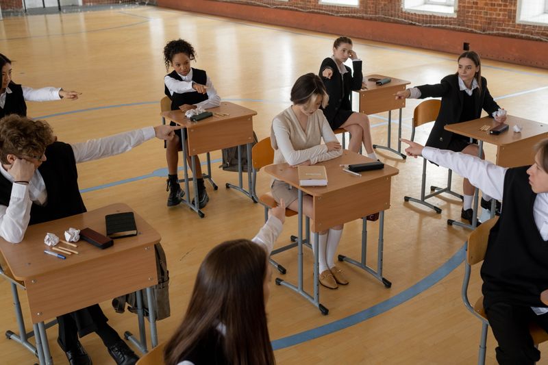 Grupo de alunos apontando e intimidando um colega de uniforme em um ambiente de sala de aula.