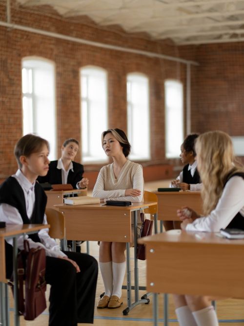 Diverse students in school uniforms discussing in brick-walled classroom