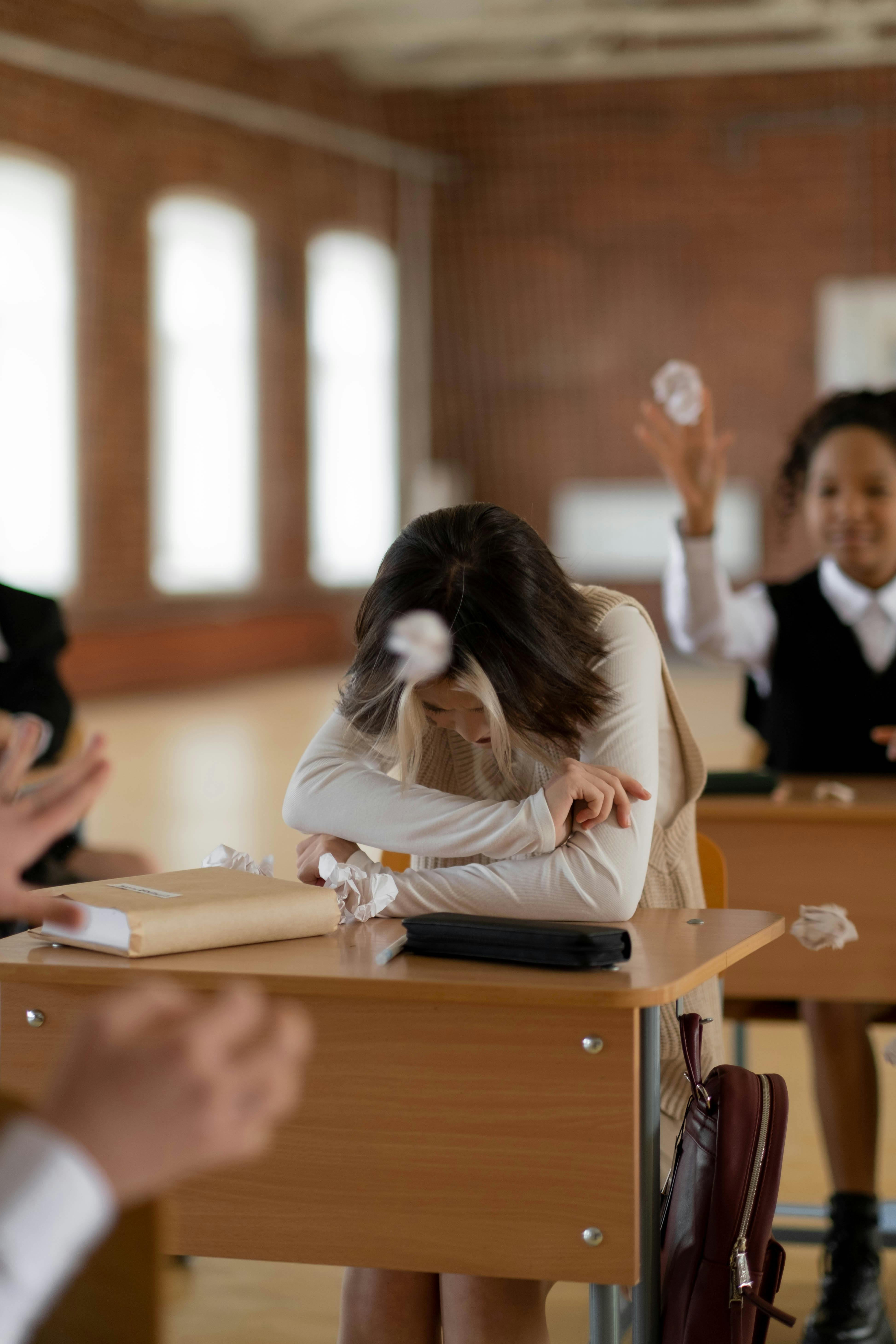 students throwing crumpled papers to a woman sitting at her desk