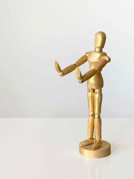 A golden wooden mannequin in a standing pose with a white backdrop.