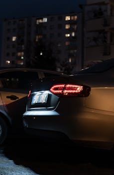 A car with illuminated tail lights parked at night in Poznań, Poland, urban setting visible in background.