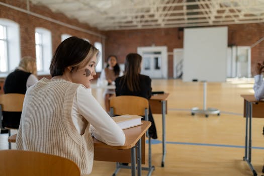 Students in a classroom, focusing on an engaged young woman with a heart-shaped birthmark on her face.