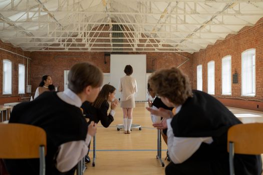 A classroom scene with students gossiping while the teacher stands at the front.