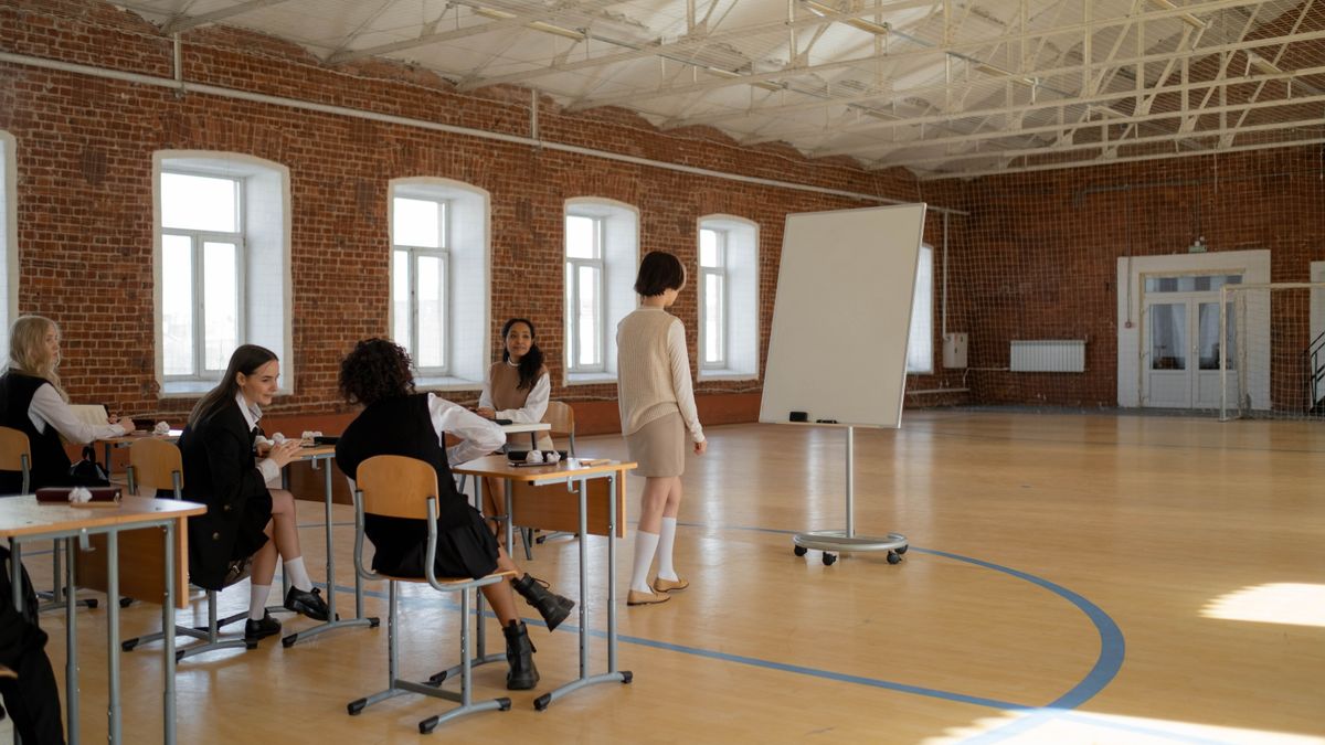 Students in school uniforms engaged in a lesson with a teacher in a spacious classroom.