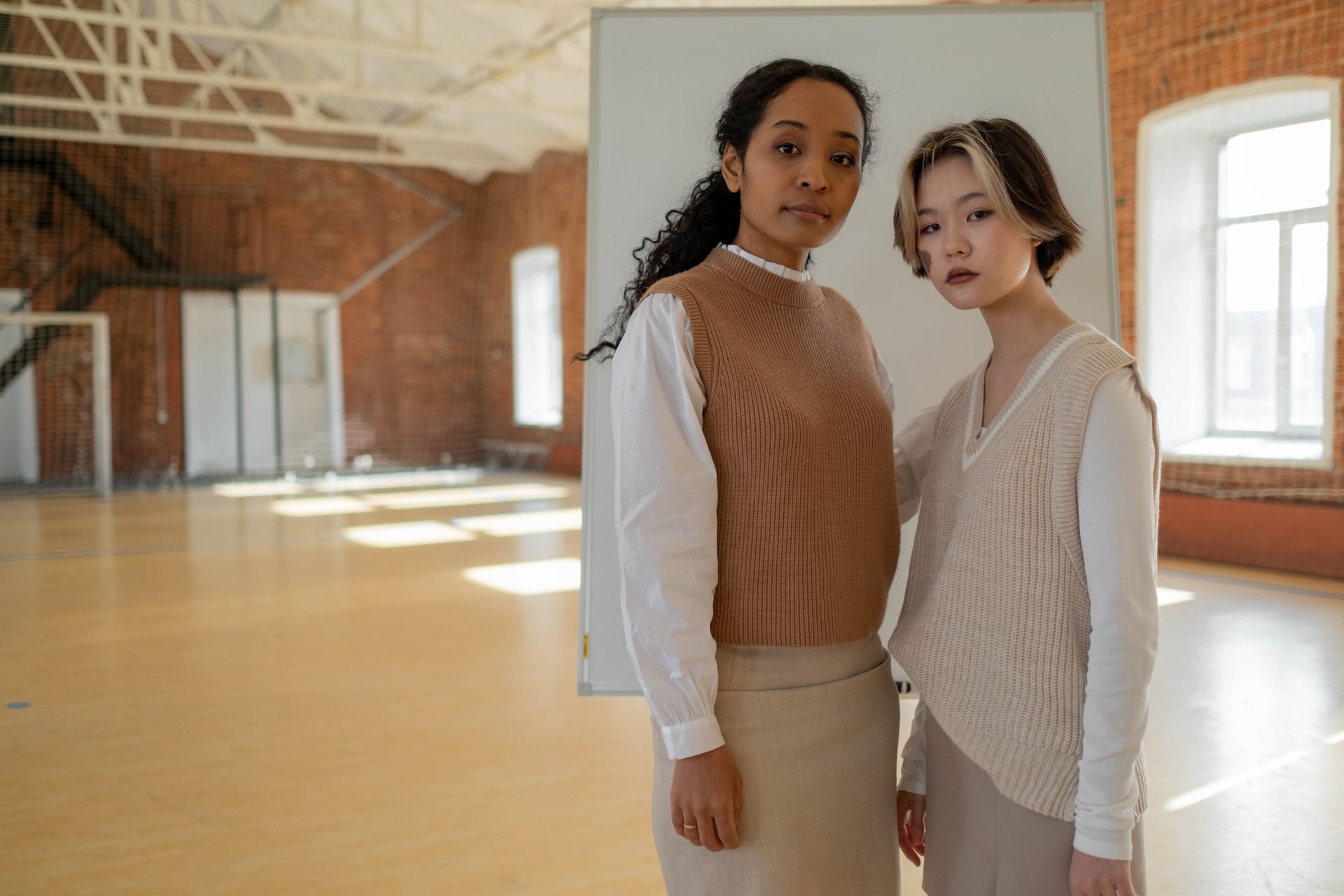 Two women standing confidently indoors, embodying education and style.