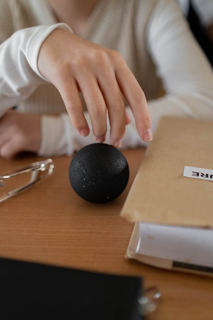 Close-up Of Woman Touching A Black Ball While Sitting At A Desk 