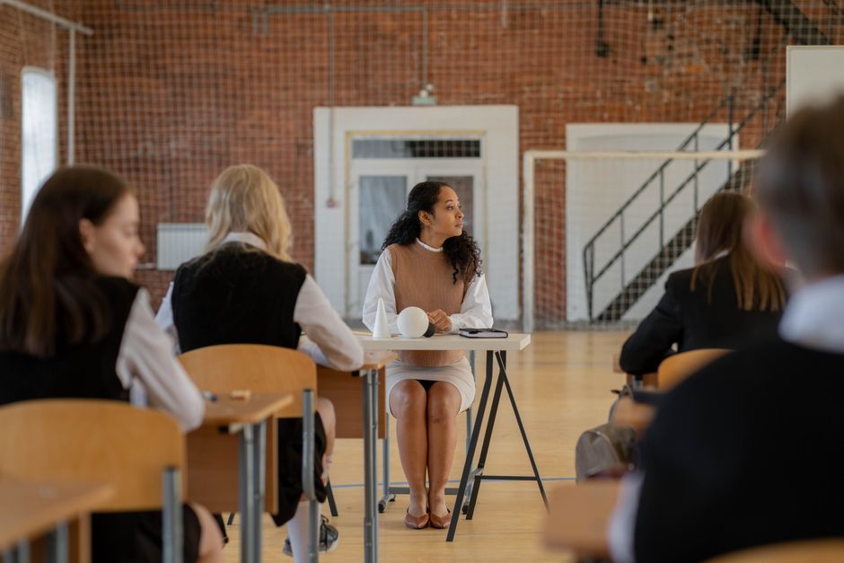 Teacher sitting at desk during class in a school gymnasium.