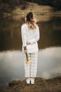 Unrecognizable trendy woman with blooming daffodils contemplating river from shore