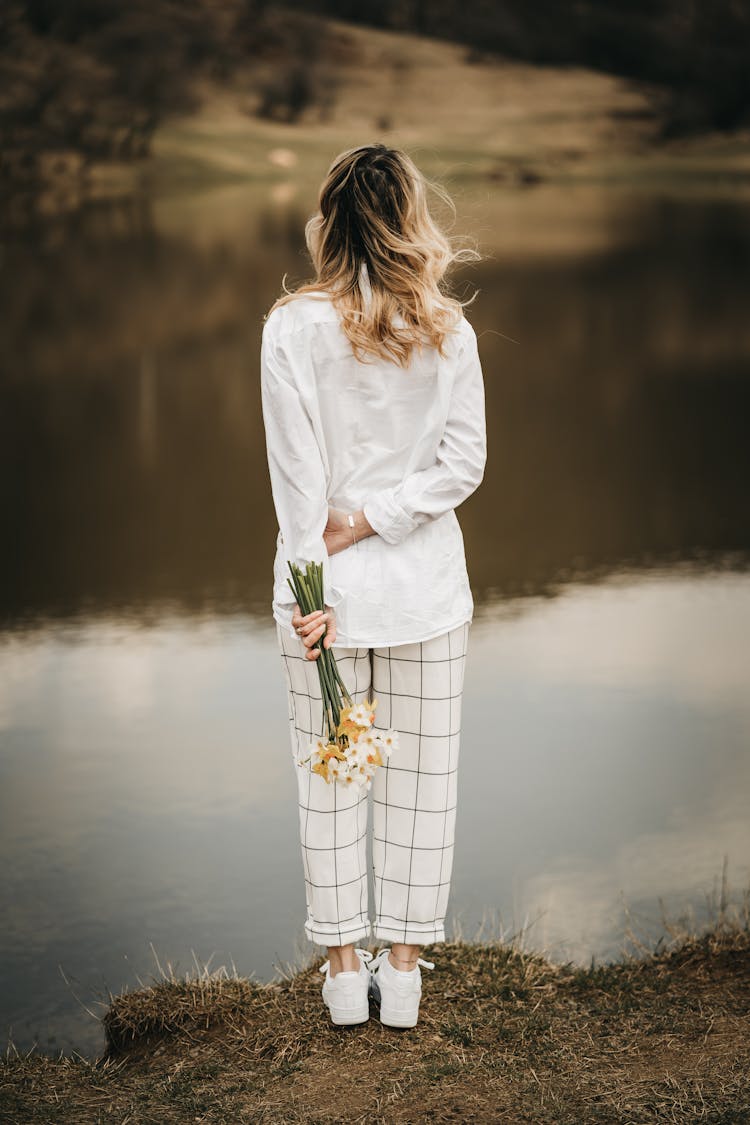 Unrecognizable Trendy Woman With Blooming Daffodils Contemplating River From Shore