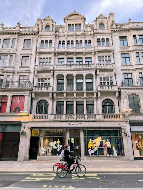 Exterior of aged building with ornamental walls and balconies in city center with people cycling down road