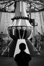Black and white back view of unrecognizable person standing near merry go round in amusement park