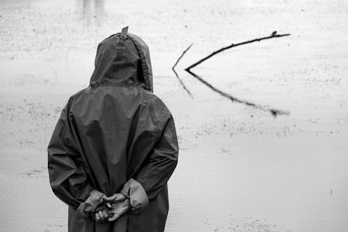 Anonymous fisherman in raincoat standing near lake in nature