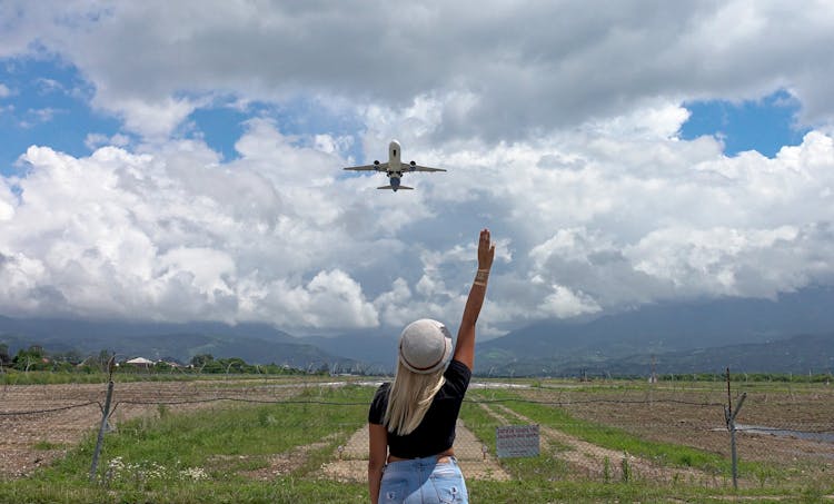 Unrecognizable Woman Standing In Field Under Flying Airplane