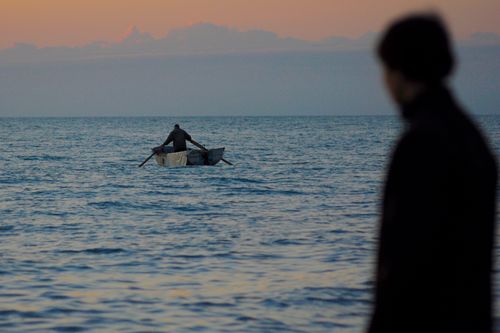Free Anonymous man observing unrecognizable male floating wooden boat in calm sea at sunset Stock Photo