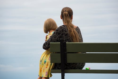 Mother and daughter sitting on bench near sea