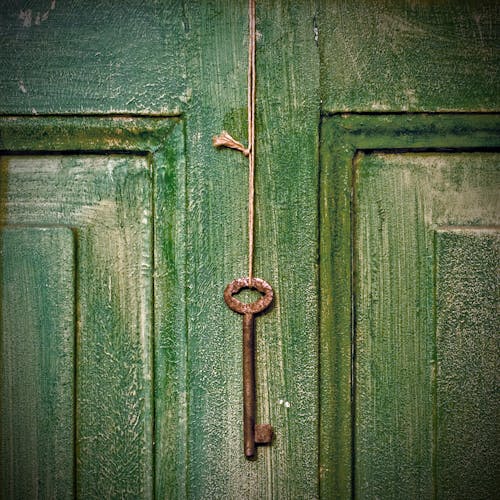 Free Weathered rusty metal key hanging on rope on shabby green wooden door of house Stock Photo