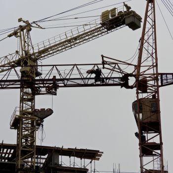 From below of metal industrial cranes located in contemporary construction site against gray sky