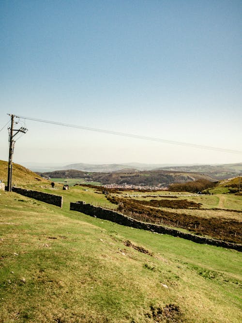 Picturesque scenery of utility line in verdant grassy hilly terrain under blue sky