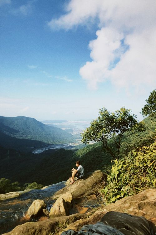 Free A lone hiker sits on a rocky ledge, gazing at a vast mountain landscape under a clear blue sky. Stock Photo