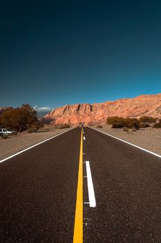 Straight asphalt road leading to rugged mountains under clear blue skies.