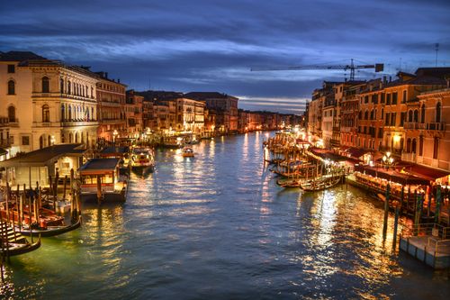 Free Stunning evening shot of Venice's Grand Canal with illuminated waterfront buildings and docked boats. Stock Photo