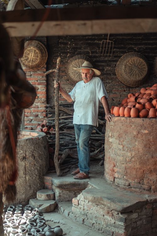 Free An elderly potter in a rustic workshop surrounded by clay pots and tools. Stock Photo